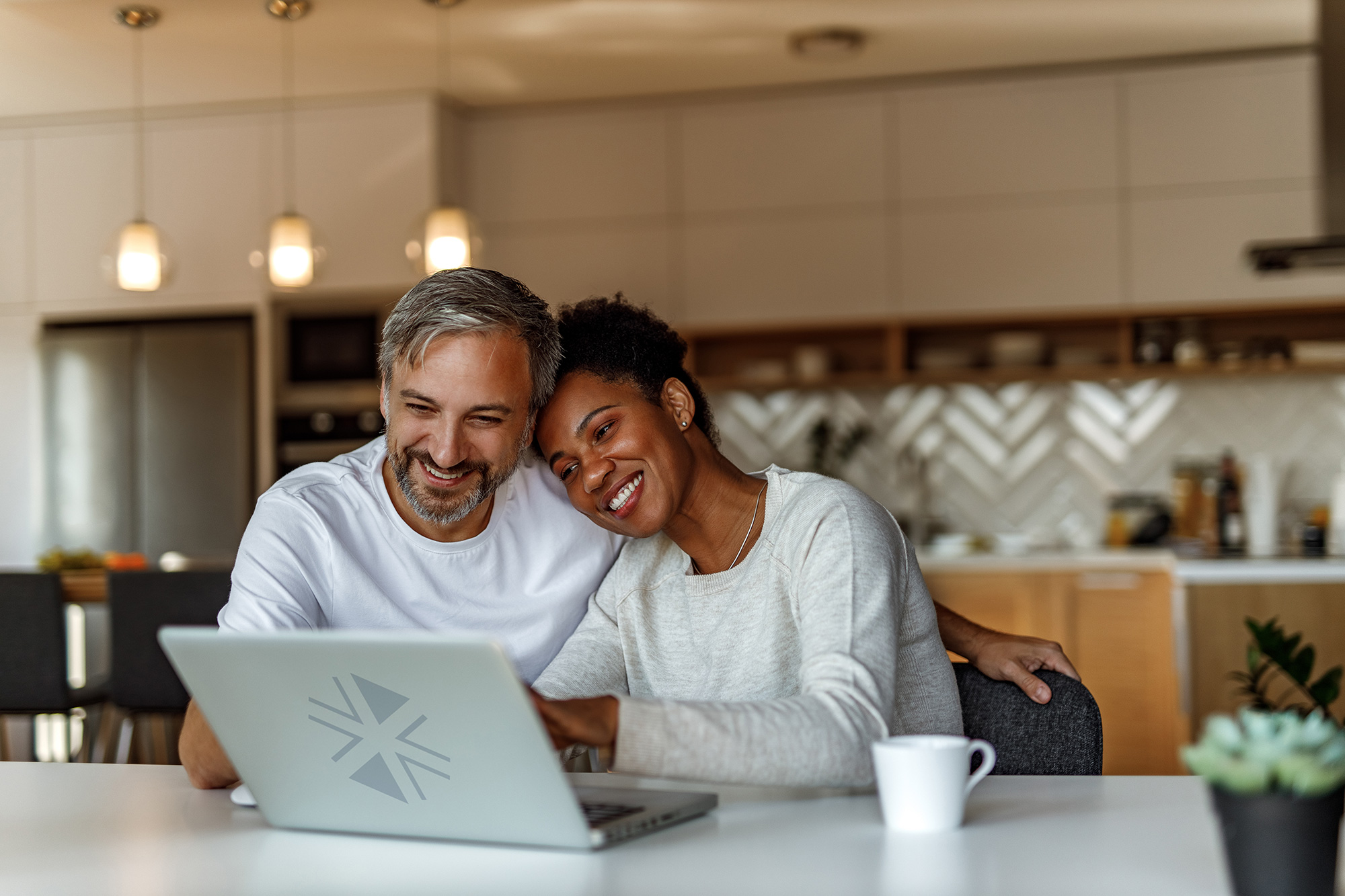 A man and woman sit together smiling and looking at a laptop in front of them.