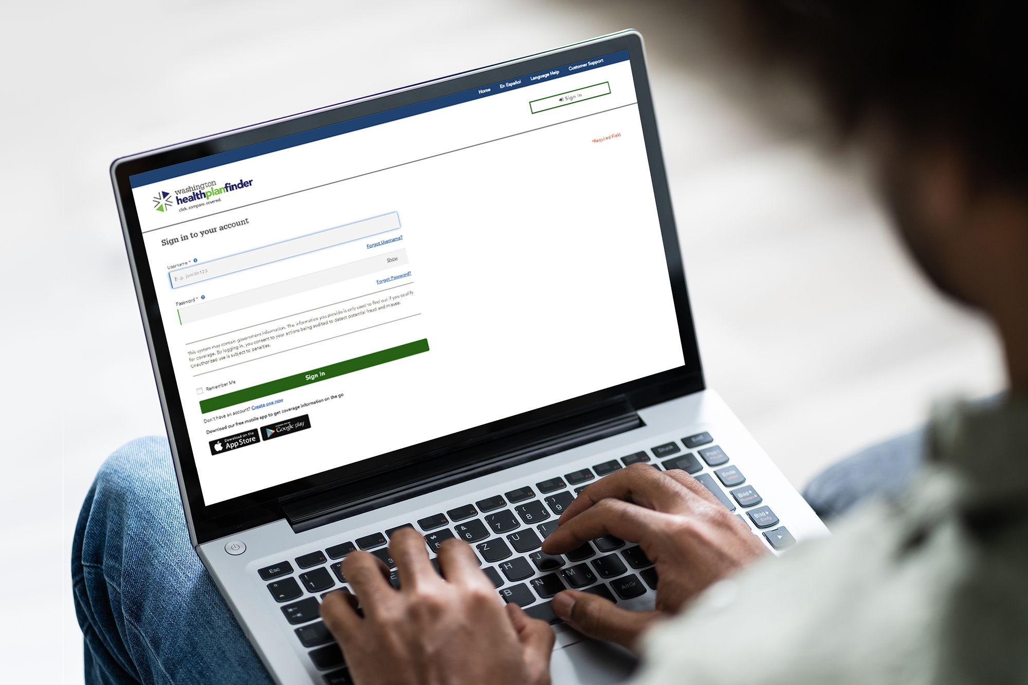 Una persona escribiendo en su computadora portátil, en donde aparece la pantalla de inicio de sesión de Washington Healthplanfinder.