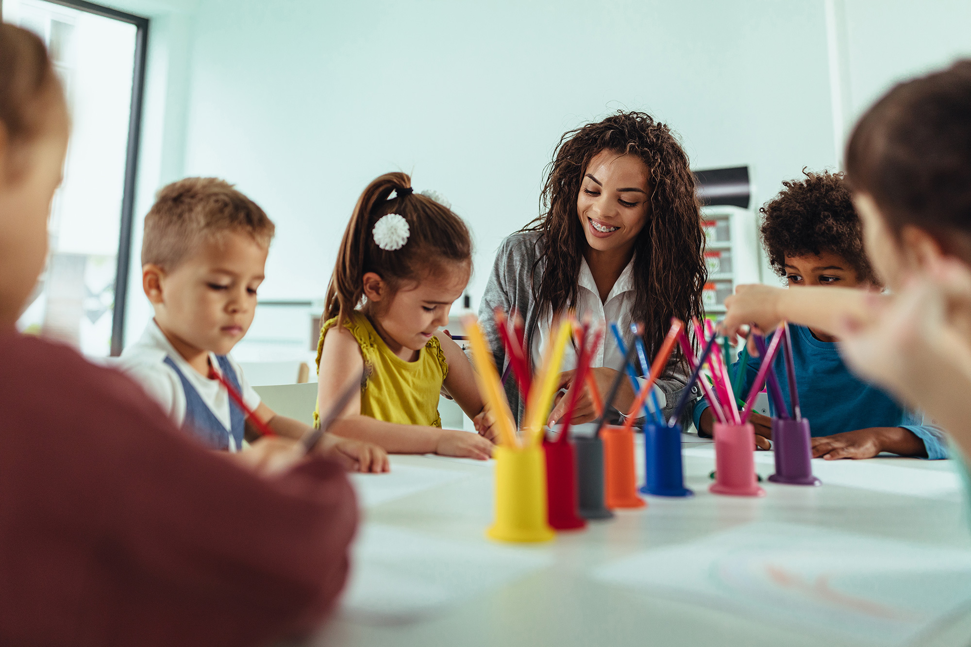 Un cuidador y sus niños dibujan con lápices de colores en una mesa