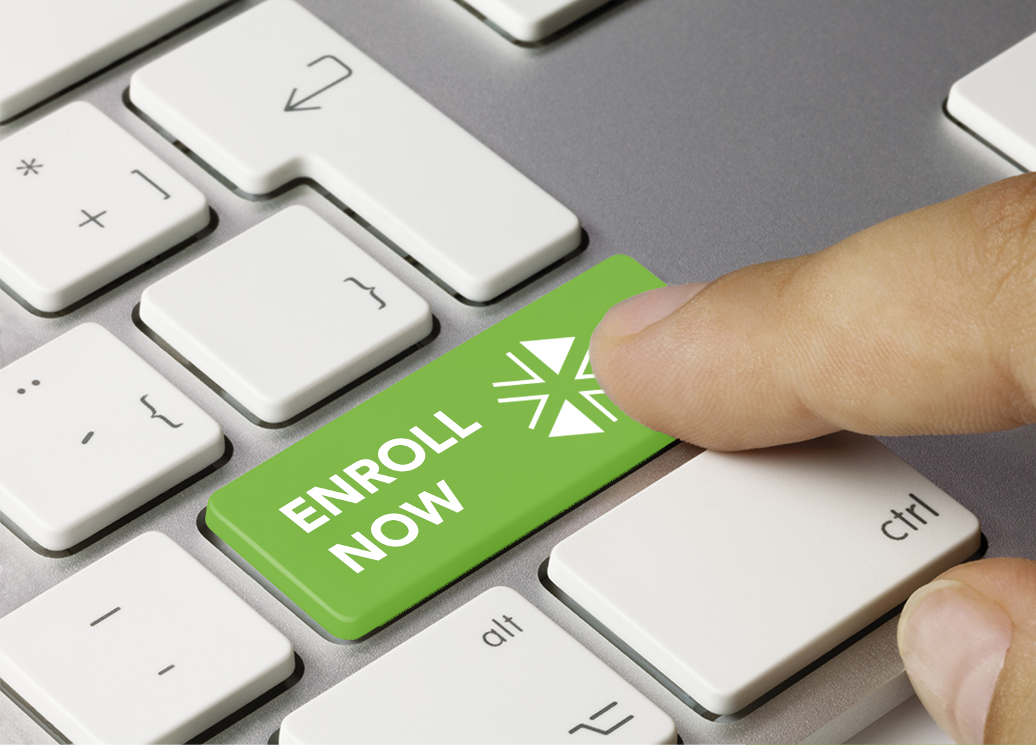 Close up of a finger pressing a key on a keyboard. The key is green and reads “Enroll Now”