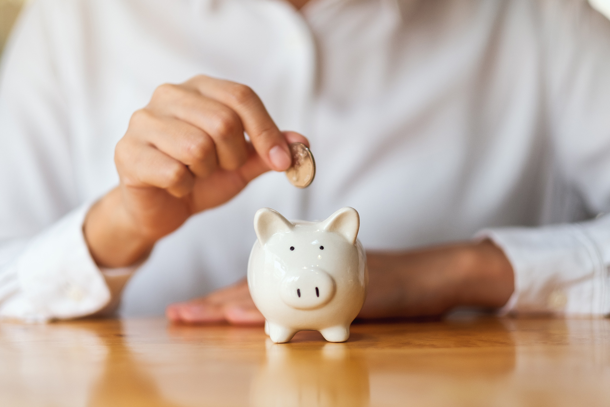 A hand holds a coin over a small, white piggy bank