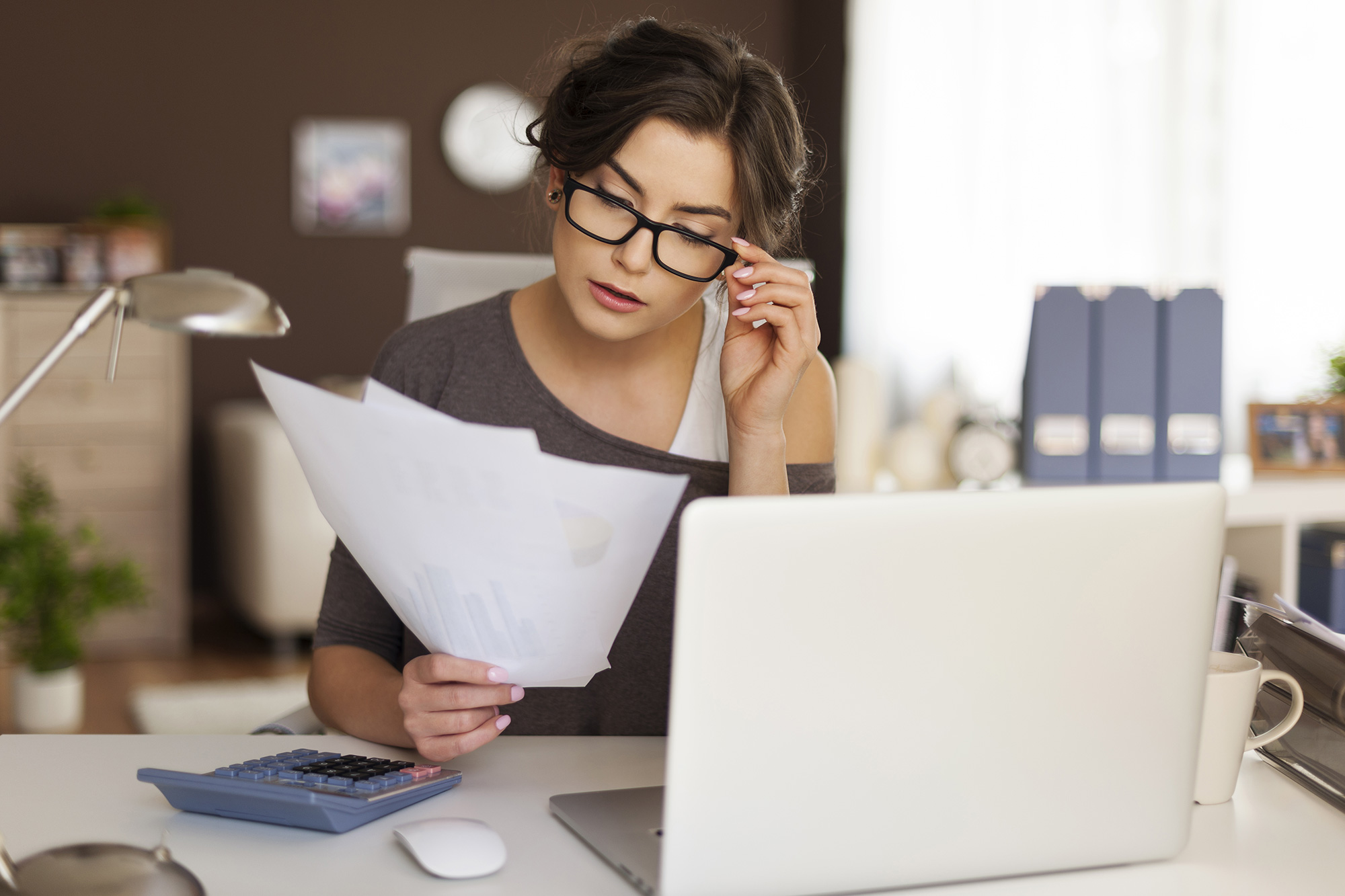 A woman reads documents in front of her laptop.