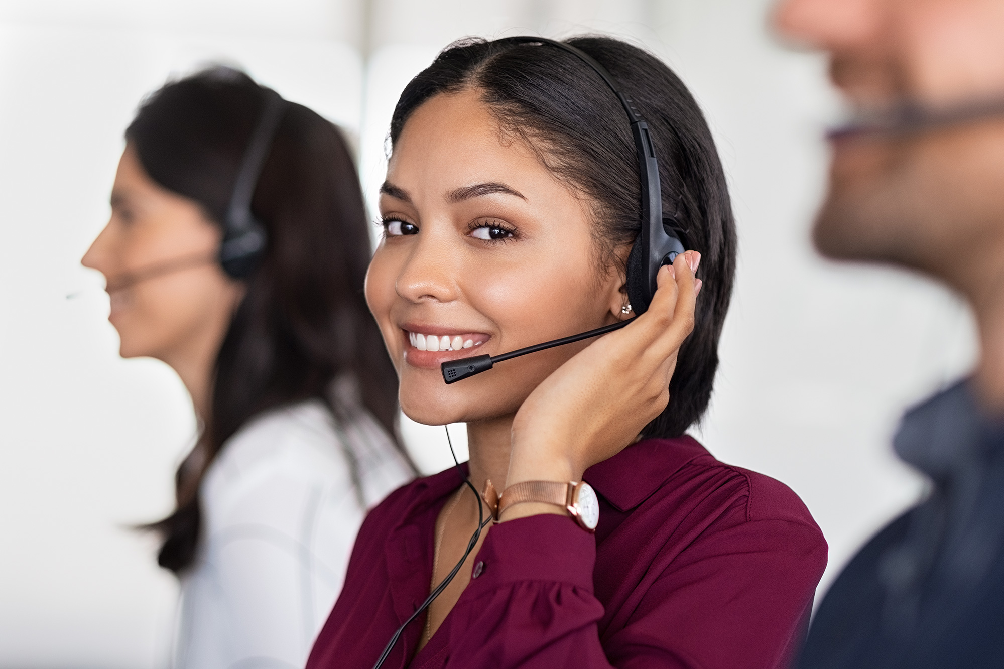 A customer service representative in a headset looks at the camera and smiles.