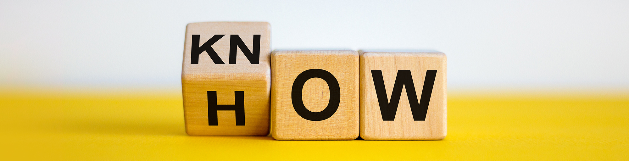 Three wooden blocks on a yellow background spelling out “Know How”